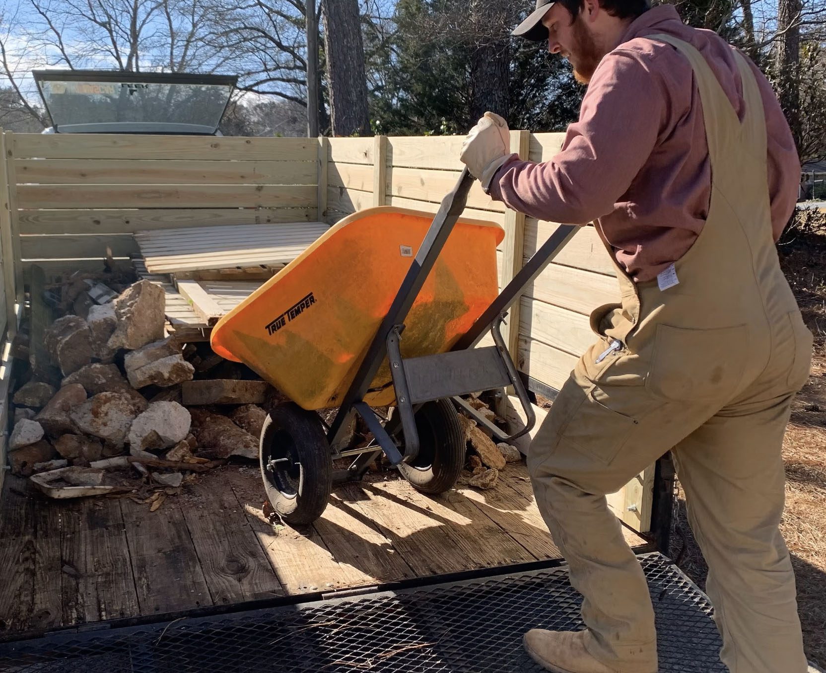 Haulin’ Ass Junk Removal worker loading construction debris into trailer with a wheelbarrow in Cherokee County.