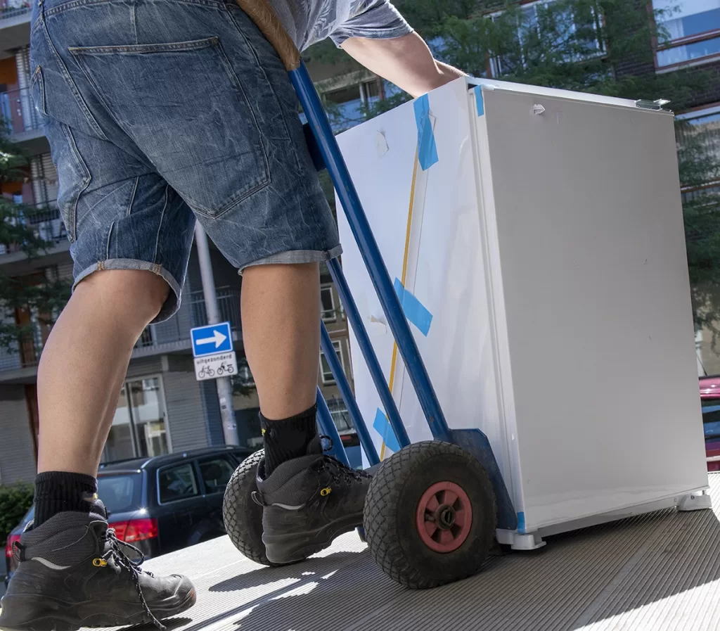 Haulin' Ass Junk Removal worker using a dolly to remove an old refrigerator in Canton GA