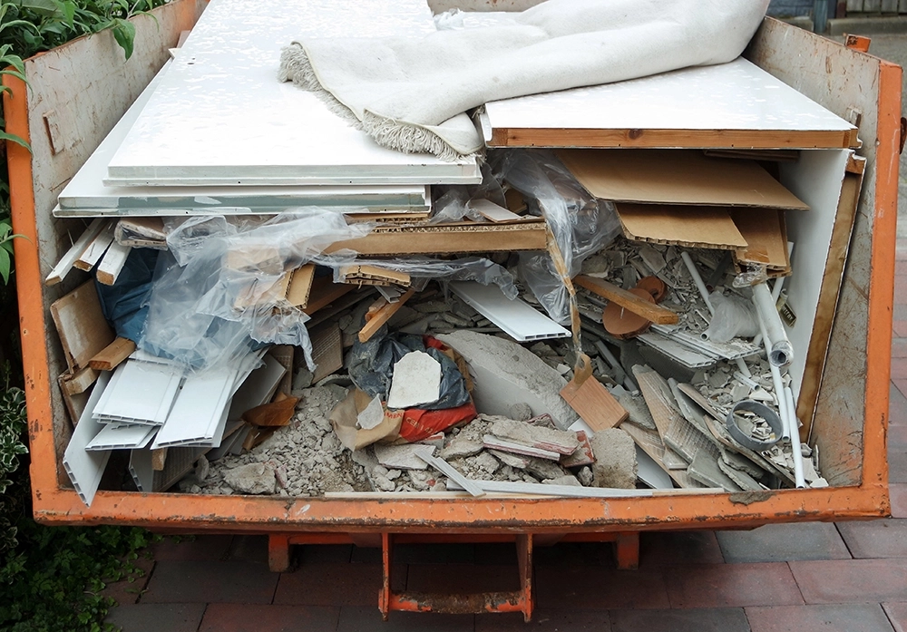 Dump trailer loaded with mixed commercial junk including drywall, concrete, tile, doors, and rugs