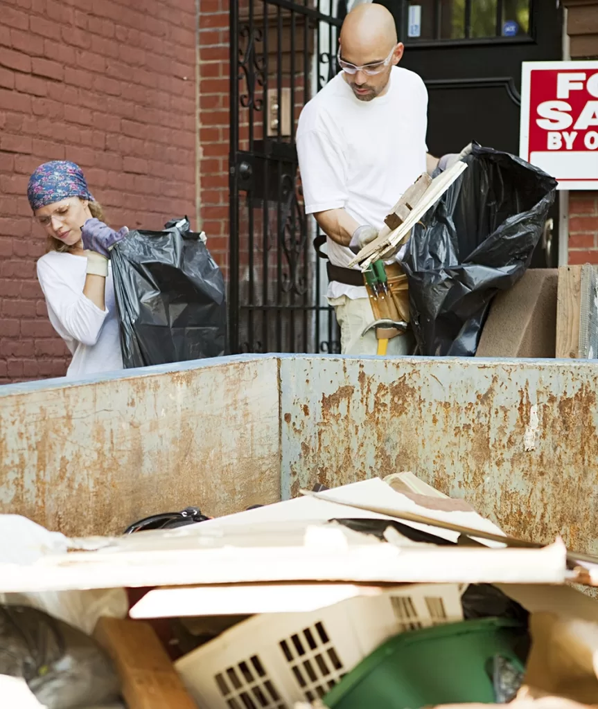 Two people clearing a home during a foreclosure cleanout, throwing items into a dumpster in Cartersville GA
