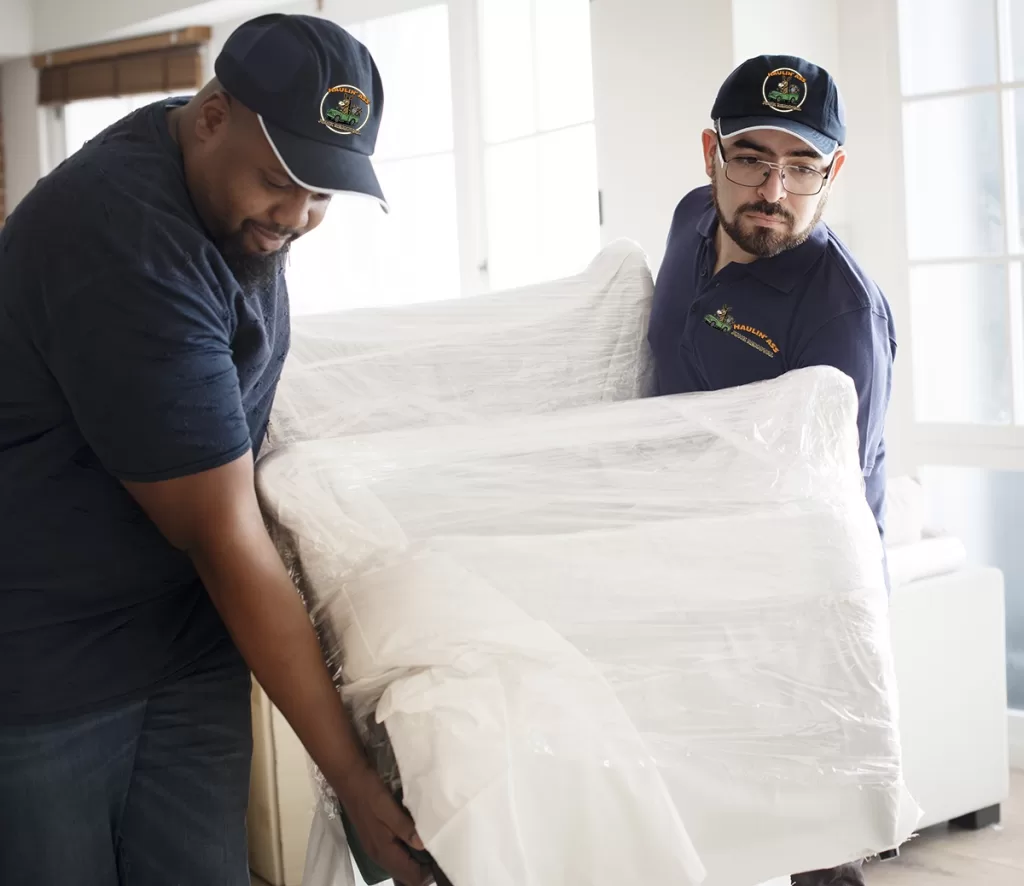 Two Haulin’ Ass workers delivering a wrapped chair to a customer’s home