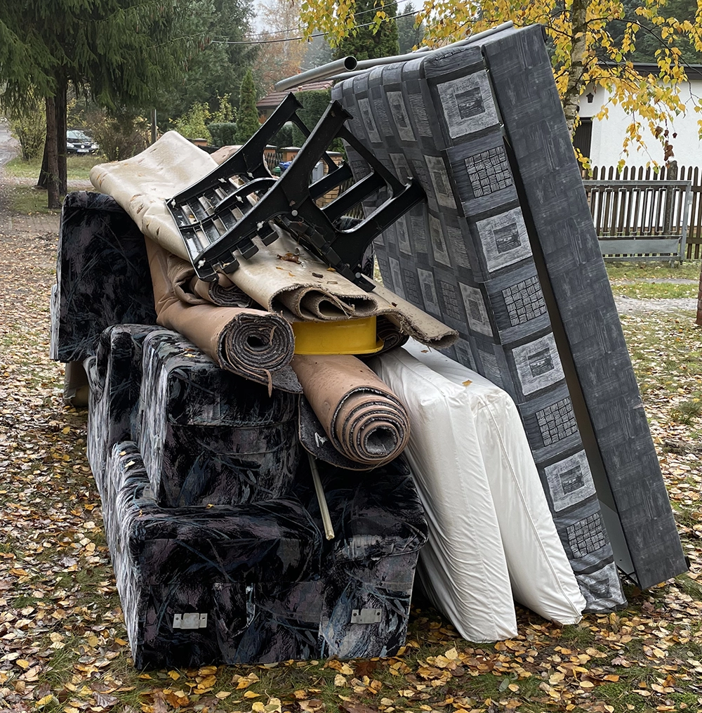 Curbside residential junk removal with old couch, carpet, mattress, and chair piled for pickup